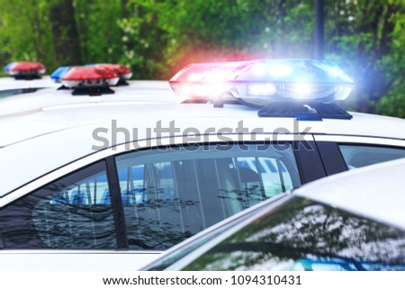 Some police cars with focus on siren lights. Beautiful siren lights activated on a police car before leaving the department park. Police cars stationed side by side, in full operation. 