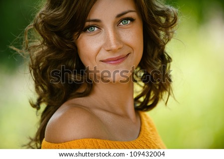 Beautiful young woman close-up in orange sweater, against green of summer park.