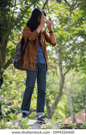 Asian male traveler carried a travel bag on back and take a photo by camera in the forest. concept of travel, trip