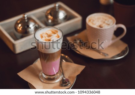 Two cups of cappuccino with latte art with a spoon and sugar bowl on wooden background. Beautiful foam, white ceramic and glass cups, stylish toning, space for text.