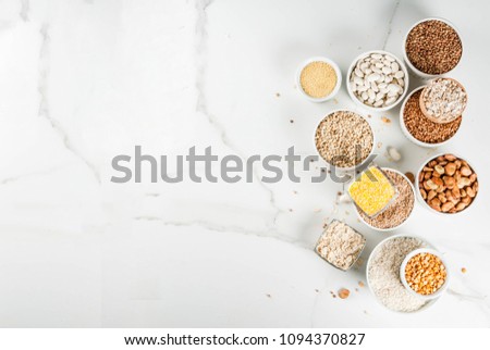 Selection various types cereal grains groats  in different bowl on white marble background, above copy space