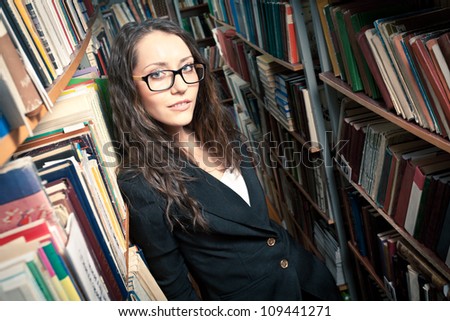 woman wearing glasses standing between bookshelves