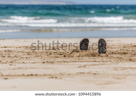 Picture of a pair of Flip-Flops in the sand with blue sea and waves on the background. La Graciosa, Lanzarote, Canary Islands, Spain.