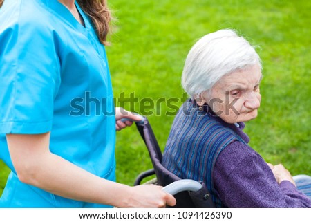 Senior disabled woman in wheelchair walking outdoor with female caretaker