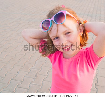 Girl in a bright pink t-shirt.Sunglasses and bracelet. Summer heat.