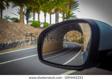 A beautiful landscape overlooking the road leading to the ocean. the road is surrounded by palm trees. Tenerife. Canary Islands. Spain. unusual photo through the car mirror with a double perspective.