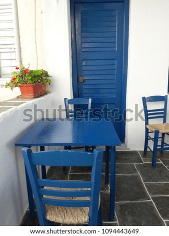 Cycladic colors; greek islands with blue and white colors. A wooden table and chairs. On the back there is also a blue wooden door. Outdoor design in Sifnos island, Greece