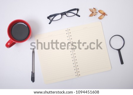 Minimalist notebook on office table desk. Workspace with notebook, spectacle, pen, magnifying glass, cup of coffee, potpourri on white background. Flat lay, top view