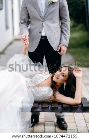 Portrait of a beautiful couple in love on your wedding day. The bride and groom enjoy each other, sitting on a bench. Amazing kisses and embraces of the bride and groom.