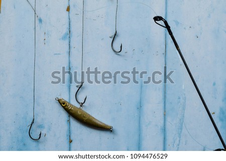 hanging fish hooks over blue colored wooden background in fishing theme