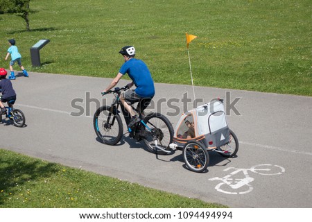 father and son on a electric bike with a bike trailer and a yellow pennant on the top enjoying the leisure time