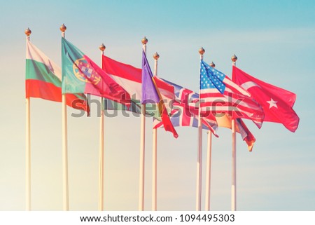 Flags of different countries on the white flagpoles flutters in the wind against a sunlight (toned) 