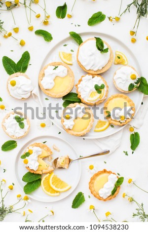 Homemade lemon curd tartlets with meringue, mint leaves and flowers on a white bacground. Top view