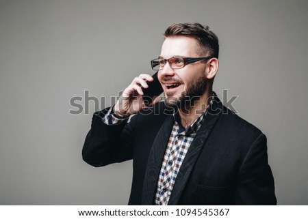 Side view shot of handsome brunette business man in casual shirt, stylish black jacket talking on the cell phone and smiling. Isolated grey background. Studio