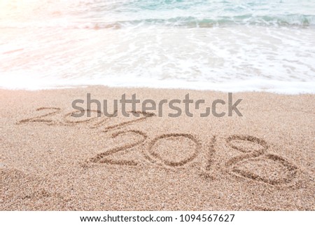 Happy new year 2018 is coming and replace 2017 concept. Number 2018 written on sandy beach with blue sea waves and foam. Holiday, vacation and new year celebration on tropical summer beach. Royalty-Free Stock Photo #1094567627