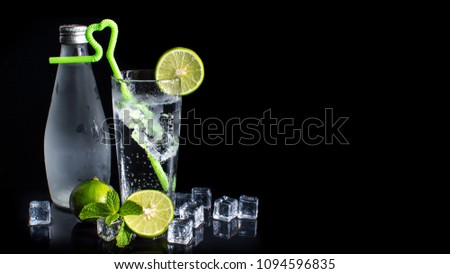 Close up of iced lemon soda glass in drinks bar isolated on black background. Cold homemade lemonade with ice and lemon. Bottles of sparkling, soda, drinking water, natural mineral water and ice cubes