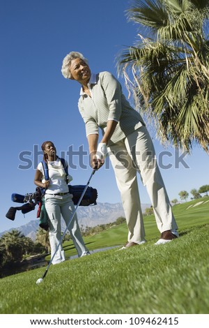 Happy female golfer playing golf with woman carrying bag in background