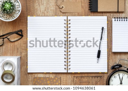 Wooden desk with open empty notebook, black clock, cactus and glasses