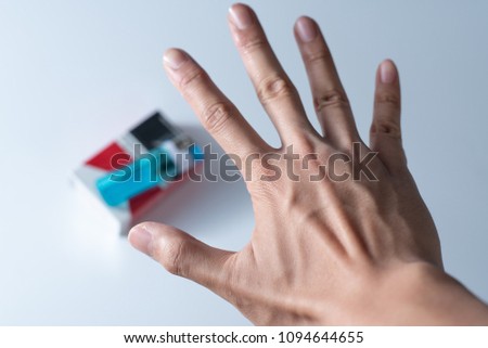 View showing a hand of a person refusing to pick up a pack of cigarettes and making a hand sign.
