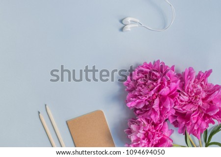 Flat lay desk with pink peonies, notebook and accessories on light blue background