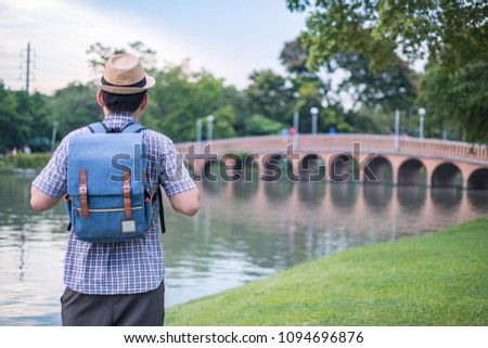asian young man age 25-30 year tourists backpacker are watching the beauty of the bridge and river in the park and tourist attractions. happily during travel the holidays and relax.