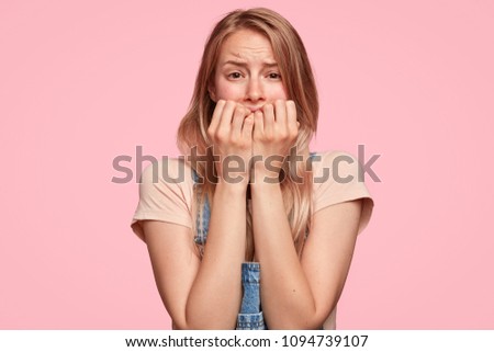Desperate Caucasian female with worried expression, bites finger nails nervously, finds out tragic news, poses against pink background. Intelligent student worries before answering on final exam Royalty-Free Stock Photo #1094739107