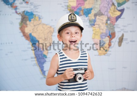 cute laughing boy in captain's hat and camera in hand on map background