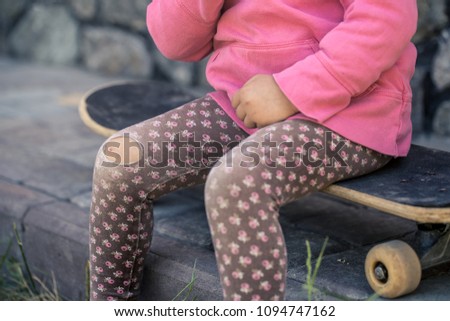 A beautiful little girl fell on skateboarding, a bruised knee injury with her hands close-up. The concept of a safe and fun childhood. Children's skateboarding.