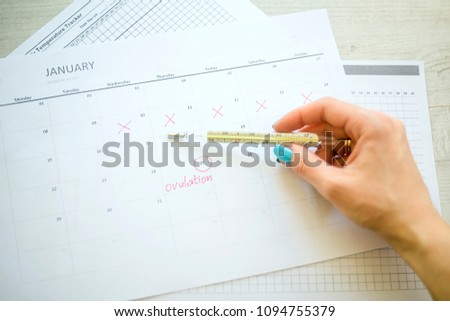 woman hand holds thermometer over calendar basal temperature , Concept of fertility chart, trying to have baby and natural contraception, Reminder Ovulation in graph, Planning of pregnancy, menstrual