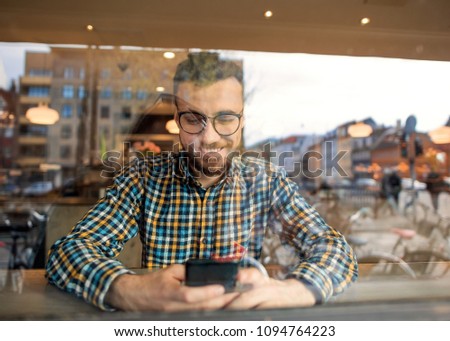 fashion guy with glasses and checkered shirt sitting in a cafe working in the phone