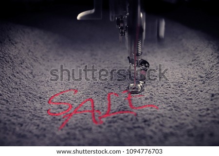embroidery of red lettering SALE on soft grey fabric with embroidery machine - detailed front view with toned light mood - background and foreground blanked out blurry - marketing and business concept