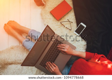 Top view of a young woman holding laptop computer on her lap while sitting at home. Woman using laptop for browsing internet store. Online shopping concept. Young woman sitting on carpet at home.