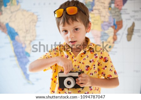 handsome boy in vivid yellow shirt with film retro camera in hands on world map background