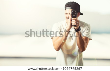 Young rapper man excited and entertained, looking through a film camera, looking for an interesting shot, recording a movie, executive producer