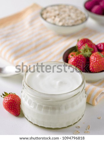 White yogurt in glass bowl and starwberries around on white background.