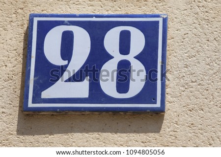 Close up outdoor view of the number twenty eight wriiten in white on a blue  rectangular metallic plate. Numerical symbol indicating a home address in a french street. Abstract image of numero 28. 