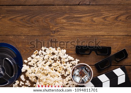 Cinema background, top view. Clapperboard, popcorn, soda and 3D glasses on wooden table, copy space. Movie goers accessories, cinematography concept