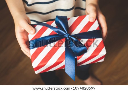 Close up view of boy holding gift box wrapped in stripes paper and tied with blue bow. Father's day background.