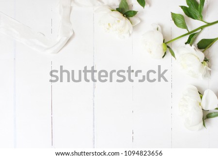 Styled stock photo. Feminine wedding table composition with white peonies flowers and silk ribbon on old white wooden background. Empty space. Top view. Picture for blog.