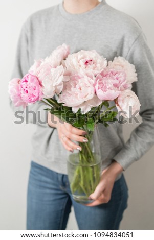 Cute and lovely peony flowers in women's hands.. many layered petals. Bunch pale pink peonies flowers light gray background.