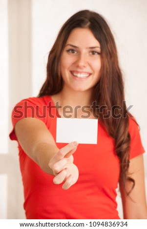 Beautiful young woman in red t shirt holds blank card over white background.