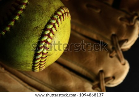 Yellow softball in a brown glove.