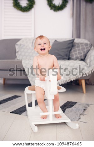 Smiling little baby playing on a wooden toy horse in cozy room.