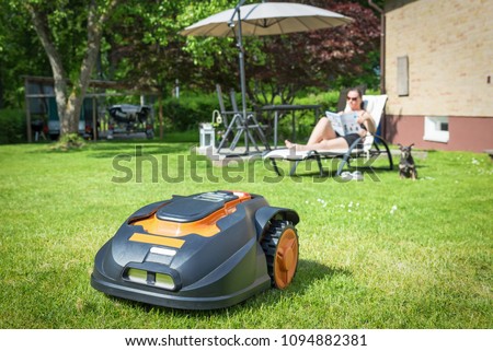 Automatic lawnmower in modern garden Royalty-Free Stock Photo #1094882381