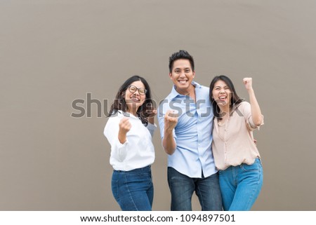 Group of happy three Asian friends in casual wear celebrating winning or success together