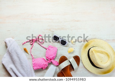 Top view of two pieces pink swimming suit and beach accessoties over wooden background. Copy space.
