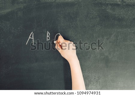 child's hand with chalk write letters a, b, c on black chalkboard, stock photo image