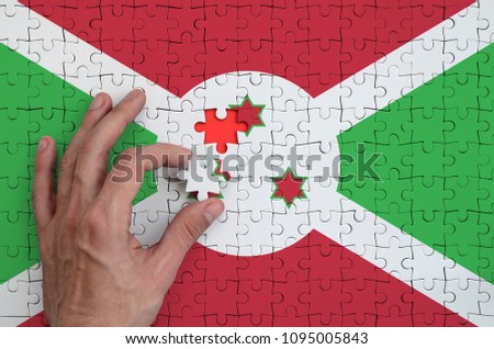 Burundi flag  is depicted on a puzzle, which the man's hand completes to fold.