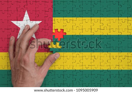 Togo flag  is depicted on a puzzle, which the man's hand completes to fold.
