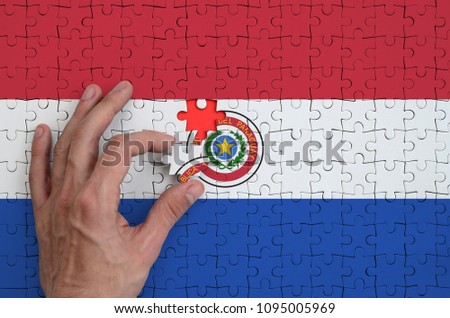 Paraguay flag  is depicted on a puzzle, which the man's hand completes to fold.